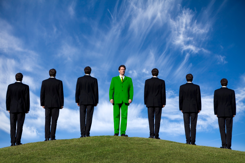 Conceptual image of businessmen on a hilltop with one dressed in green suit looking in the opposite direction. Environmental concern issues - how green are you? Looking for a greener future etc.